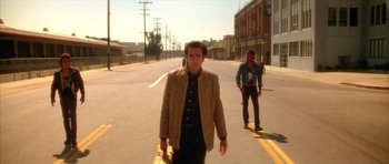 Movie still from “Wild at Heart” (1990), directed by David Lynch – A man walking down a street with a skateboard; Wide shot, Low angle