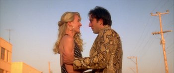 Movie still from “Wild at Heart” (1990), directed by David Lynch – A man and a woman holding each other in front of a sky background; Medium shot, Low angle