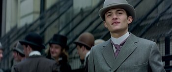 Movie still from “Wilde” (1997), directed by Brian Gilbert – A young man in a suit and a hat is standing in front of a group of people; Close Up shot, Low angle