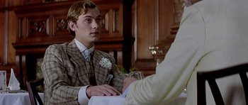 Movie still from “Wilde” (1997), directed by Brian Gilbert – A man in a suit and tie sitting in front of a person; Close Up shot, Over the shoulder angle