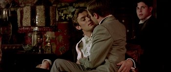 Movie still from “Wilde” (1997), directed by Brian Gilbert – A couple of men sitting on top of each other; Medium shot, Over the shoulder angle