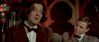 Movie still from “Wilde” (1997), directed by Brian Gilbert – A man with long hair and a bow tie; Close Up shot, Over the shoulder angle