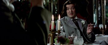 Movie still from “Wilde” (1997), directed by Brian Gilbert – A man sitting at a dinner table with candles in front of him; Close Up shot, Over the shoulder angle