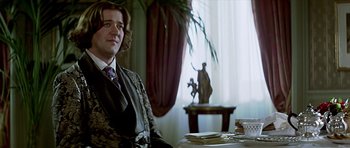 Movie still from “Wilde” (1997), directed by Brian Gilbert – A man sitting at a table with plates of food in front of him; Medium shot, Low angle