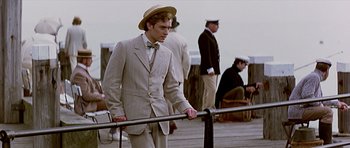 Movie still from “Wilde” (1997), directed by Brian Gilbert – A man in a suit and hat standing next to a railing; Medium shot, Low angle