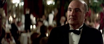 Movie still from “Wilde” (1997), directed by Brian Gilbert – A man in a tuxedo standing in front of a group of people; Close Up shot, Over the shoulder angle