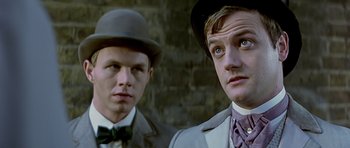 Movie still from “Wilde” (1997), directed by Brian Gilbert – Two men in suits and hats are standing next to a brick wall; Close Up shot, Low angle