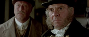 Movie still from “Wilde” (1997), directed by Brian Gilbert – An old man with a beard wearing a top hat; Close Up shot, Over the shoulder angle