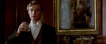 Movie still from “Wilde” (1997), directed by Brian Gilbert – A man in a suit and bow tie standing in front of a painting; Medium shot, Low angle