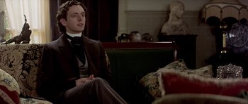 Movie still from “Wilde” (1997), directed by Brian Gilbert – A man sitting on top of a couch in a living room; Medium shot, Low angle