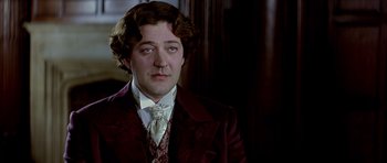 Movie still from “Wilde” (1997), directed by Brian Gilbert – A man in a suit and tie in a dark room; Close Up shot, Over the shoulder angle