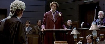 Movie still from “Wilde” (1997), directed by Brian Gilbert – A man standing at a podium in front of a group of people; Medium shot, Low angle
