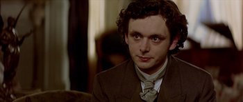 Movie still from “Wilde” (1997), directed by Brian Gilbert – A man in a suit and tie sitting in a chair; Close Up shot, Over the shoulder angle