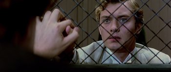 Movie still from “Wilde” (1997), directed by Brian Gilbert – A man sitting in front of a chain link fence; Close Up shot, Over the shoulder angle