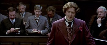 Movie still from “Wilde” (1997), directed by Brian Gilbert – A man wearing a suit and tie in a courtroom; Medium shot, Low angle