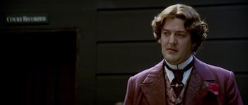 Movie still from “Wilde” (1997), directed by Brian Gilbert – A man in a suit and tie standing in front of a building; Close Up shot, Over the shoulder angle