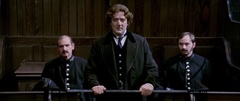 Movie still from “Wilde” (1997), directed by Brian Gilbert – A man standing in front of two other men; Medium shot, Low angle