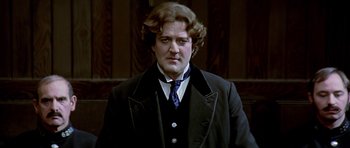 Movie still from “Wilde” (1997), directed by Brian Gilbert – A man in a suit and tie standing in front of a wooden wall; Close Up shot, High angle