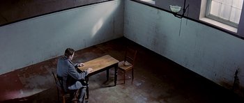 Movie still from “Wilde” (1997), directed by Brian Gilbert – A man sitting at a table in an empty room; Wide shot, High angle