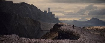 Movie still from “Willow” (1988), directed by Ron Howard – A person standing on top of a mountain near a castle; Extreme Wide shot, High angle