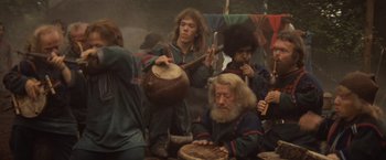 Movie still from “Willow” (1988), directed by Ron Howard – A group of people gathered around a man playing an instrument; Wide shot, High angle