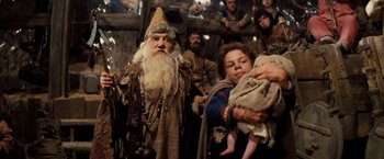 Movie still from “Willow” (1988), directed by Ron Howard – A man dressed as an old man holding a baby; Medium shot, Over the shoulder angle
