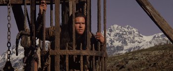 Movie still from “Willow” (1988), directed by Ron Howard – A man is looking through the bars of a prison cell; Medium shot, Low angle