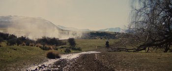 Movie still from “Willow” (1988), directed by Ron Howard – A person riding a horse on a dirt road near a field; Extreme Wide shot, Low angle