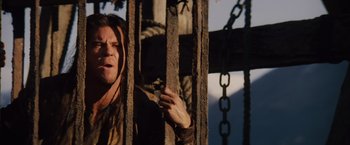 Movie still from “Willow” (1988), directed by Ron Howard – A man standing next to a chain link fence; Close Up shot, Low angle