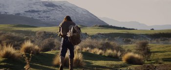 Movie still from “Willow” (1988), directed by Ron Howard – A person with a backpack walking in a field; Wide shot, Low angle