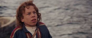 Movie still from “Willow” (1988), directed by Ron Howard – A young boy is standing in front of a body of water; Close Up shot, High angle