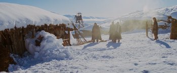 Movie still from “Willow” (1988), directed by Ron Howard – A group of people standing in the snow near a wooden structure; Extreme Wide shot, Low angle