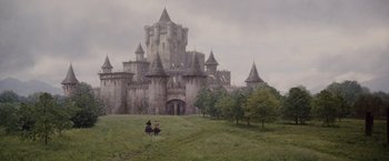 Two people riding horses in front of a castle