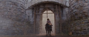 Movie still from “Willow” (1988), directed by Ron Howard – A man riding a horse through a stone gate; Wide shot, Low angle
