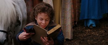 Movie still from “Willow” (1988), directed by Ron Howard – A young boy is reading a book outside; Medium shot, High angle
