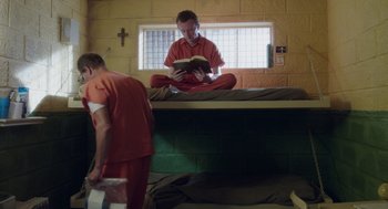 Movie still from “Wilson” (2017), directed by Craig Johnson – Two men in orange jumpsuits are reading a book on a bunk bed; Wide shot, High angle