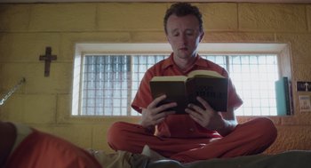 Movie still from “Wilson” (2017), directed by Craig Johnson – A man sitting on the floor reading a book; Medium shot, Low angle