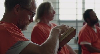 Movie still from “Wilson” (2017), directed by Craig Johnson – A man reading a book while sitting next to another man; Close Up shot, Over the shoulder angle