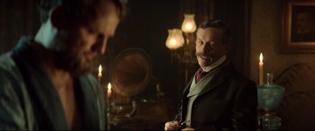 Movie still from “Winchester” (2018), directed by Michael Spierig – A man in a suit and tie standing next to another man in a suit; Medium shot, Over the shoulder angle