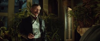 Movie still from “Winchester” (2018), directed by Michael Spierig – An older man in a suit and tie holding a pair of glasses; Medium shot, Low angle