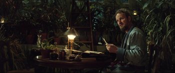 Movie still from “Winchester” (2018), directed by Michael Spierig – A man sitting at a table with a lit candle in front of him; Medium shot, Over the shoulder angle