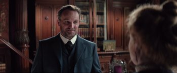 Movie still from “Winchester” (2018), directed by Michael Spierig – A man wearing a suit and tie in a room; Close Up shot, Over the shoulder angle
