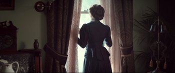 Movie still from “Winchester” (2018), directed by Michael Spierig – A woman standing in front of a window looking outside; Medium shot, Low angle