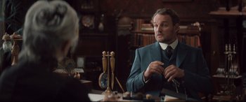 Movie still from “Winchester” (2018), directed by Michael Spierig – A man sitting at a table in front of a clock; Medium shot, Over the shoulder angle