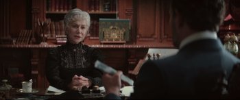 Movie still from “Winchester” (2018), directed by Michael Spierig – An older woman sitting at a table with a remote control; Medium shot, Over the shoulder angle