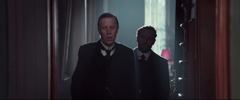 Movie still from “Winchester” (2018), directed by Michael Spierig – A man in a suit and tie standing next to another man in a suit and tie; Medium shot, Low angle