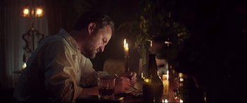 Movie still from “Winchester” (2018), directed by Michael Spierig – A man sitting at a table with a lit candle in front of him; Medium shot, Low angle
