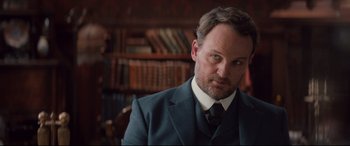 Movie still from “Winchester” (2018), directed by Michael Spierig – A person wearing a suit and tie; Close Up shot, Over the shoulder angle