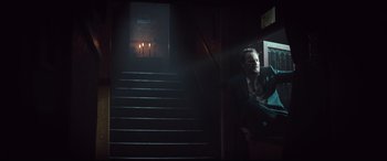 Movie still from “Winchester” (2018), directed by Michael Spierig – A man standing in a dark room next to a staircase; Wide shot, Low angle
