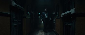 Movie still from “Winchester” (2018), directed by Michael Spierig – A man in a suit and tie walking down a hall way; Wide shot, Low angle